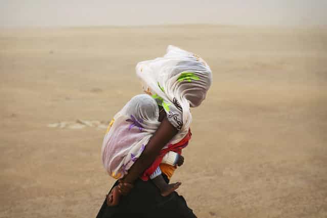A woman carrying her baby and wrapped with a shawl walks through a sandstorm in Timbuktu July 29, 2013. (Photo by Joe Penney/Reuters)