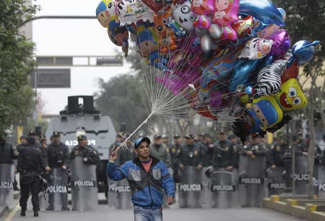 A balloon vendor walks in front of a group of riot police standing guard during an anti-government demonstration that was taking place as Peru's President Ollanta Humala delivered his State of the Nation address, in Lima, Peru, Sunday, July 28, 2013. Demonstrators claim Humala has not delivered on his promises to reduce crime and they say the political system does not represent them. (Photo by Martin Mejia/AP Photo)