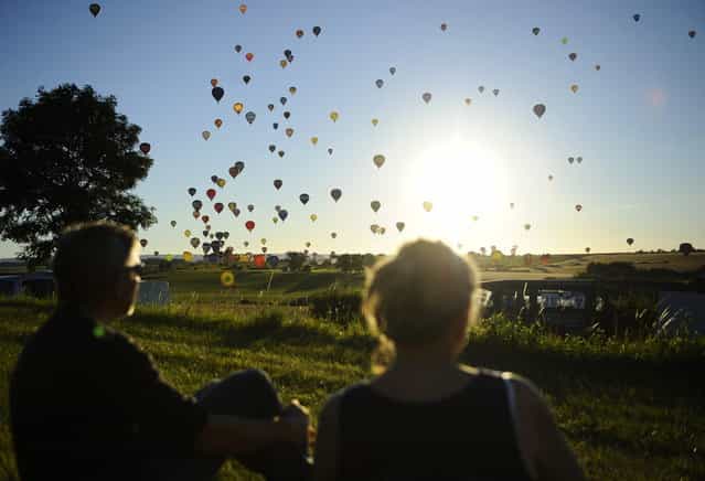 People watch hot-air balloons fly over Chambley-Bussieres, eastern France, on July 31, 2013, to try to set a world record with 408 balloons in the sky, as part of the yearly event [Lorraine Mondial Air Ballons], an international air-balloon meeting. (Photo by Jean-Christophe Verhaegen/AFP Photo)
