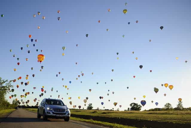 A car drives on a road while hot-air balloons fly over Chambley-Bussieres, eastern France, on July 31, 2013, to try to set a world record with 408 balloons in the sky, as part of the yearly event [Lorraine Mondial Air Ballons], an international air-balloon meeting. (Photo by Jean-Christophe Verhaegen/AFP Photo)