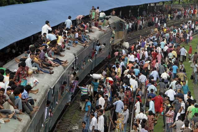 Bangladeshi passengers sit on the roof of an overcrowded train as others wait on the platform as they try to reach their homes to celebrate Eid al-Fitr in Dhaka, Bangladesh, Wednesday, August 7, 2013. Muslims across the world are preparing for the arrival of Eid al-Fitr, the festival marking the end of the Muslim fasting month of Ramadan. (Photo by A.M. Ahad/AP Photo)