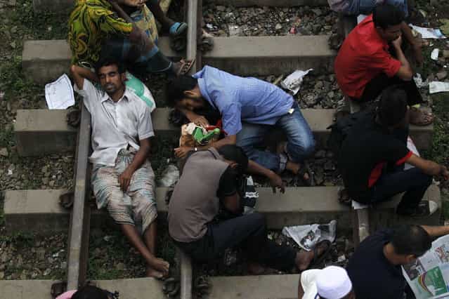 Passengers sleep on a railway track as they wait to board a train at a railway station in Dhaka, August 8, 2013. Millions of residents in Dhaka are travelling home from the capital city to celebrate the Muslim Eid al-Fitr holiday, which marks the end of the holy fasting month of Ramadan. (Photo by Andrew Biraj/Reuters)