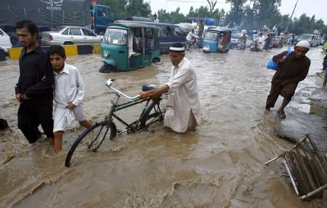 People and vehicles pass on a road flooded by heavy territorial rains in Peshawar, Pakistan, Saturday, August 3, 2013. About a dozen of people have been killed and many others injured in flash floods triggered by heavy territorial rains in Pakistan, as authorities warned the situation may worsen further. (Photo by Mohammad Sajjad/AP Photo)