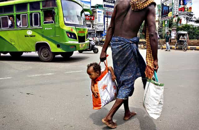 A man carries his child in a bag as he crosses a street in Bhubaneswar, India, on August 9, 2013. (Photo by Biswaranjan Rout/Associated Press)