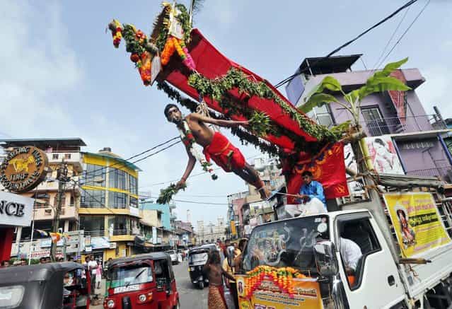 A truck carries a Sri Lankan Hindu devotee hanging with iron hooks pierced into his back as a ritual during a Hindu temple festival in Colombo, Sri Lanka, Friday, August 9, 2013. Hindu devotees mark [Paal Kudam] or the festival of milk by pouring milk on the idols of their deity and seek their blessings. (Photo by Eranga Jayawardena/AP Photo)