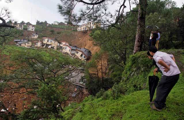 People look at buildings damaged by a landslide in Dharmsala, India, on August 7, 2013. Fearing more landslides, the nearby village of 60 residents were evacuated. No injuries were reported. (Photo by Ashwini Bhatia/Associated Press)