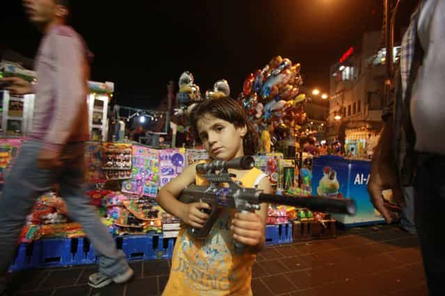 A Palestinian child poses with a plastic toy gun in front of a stall as families shop at a market on the eve of the Eid al-Fitr holiday that marks the end of the Muslim fasting month of Ramadan, on August 7, 2013 in the West Bank city of Ramallah. (Photo by Abbas Momani/AFP Photo)