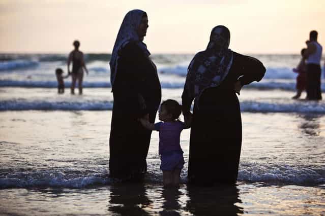 Muslim women and a toddler stand in the shallow water of the Mediterranean at a beach in Tel Aviv during Eid al-Fitr, which marks the end of the holy month of Ramadan August 10, 2013. The Israeli Coordinator for Government Activities in the Territories' (COGAT) responsible for implementing Israel's civilian policy in the occupied West Bank and Gaza Strip, eased permit restrictions for thousands of Palestinians wanting to enter Israel following a security assessment, allowing many to enjoy the beaches along Israel's Mediterranean shoreline during the Eid al-Fitr holiday. (Photo by Nir Elias/Reuters)