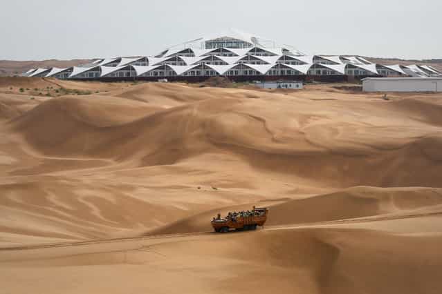 Tourists ride past the Desert Lotus Hotel under construction in Xiangshawan Desert, also called Sounding Sand Desert on July 17, 2013 in Ordos of Inner Mongolia Autonomous Region, China. Xiangshawan is China's famous tourist resort in the desert. It is located along the middle section of Kubuqi Desert on the south tip of Dalate League under Ordos City. Sliding down from the 110-metre-high, 45-degree sand hill, running a course of 200 metres, the sands produce the sound of automobile engines, a natural phenomenon that nobody can explain. (Photo by Feng Li/Getty Images)
