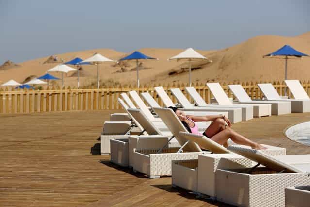 A woman rest beside a swimming pool in Xiangshawan Desert, also called Sounding Sand Desert on July 20, 2013 in Ordos of Inner Mongolia Autonomous Region, China. Xiangshawan is China's famous tourist resort in the desert. It is located along the middle section of Kubuqi Desert on the south tip of Dalate League under Ordos City. Sliding down from the 110-metre-high, 45-degree sand hill, running a course of 200 metres, the sands produce the sound of automobile engines, a natural phenomenon that nobody can explain. (Photo by Feng Li/Getty Images)