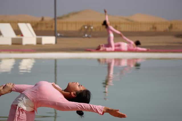 Dancers perform yoga near a swimming pool in Xiangshawan Desert, also called Sounding Sand Desert on July 20, 2013 in Ordos of Inner Mongolia Autonomous Region, China. Xiangshawan is China's famous tourist resort in the desert. It is located along the middle section of Kubuqi Desert on the south tip of Dalate League under Ordos City. Sliding down from the 110-metre-high, 45-degree sand hill, running a course of 200 metres, the sands produce the sound of automobile engines, a natural phenomenon that nobody can explain. (Photo by Feng Li/Getty Images)