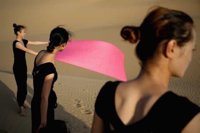 Dancers prepare for performing yoga on the dunes of Xiangshawan Desert, also called Sounding Sand Desert on July 20, 2013 in Ordos of Inner Mongolia Autonomous Region, China. Xiangshawan is China's famous tourist resort in the desert. It is located along the middle section of Kubuqi Desert on the south tip of Dalate League under Ordos City. Sliding down from the 110-metre-high, 45-degree sand hill, running a course of 200 metres, the sands produce the sound of automobile engines, a natural phenomenon that nobody can explain. (Photo by Feng Li/Getty Images)