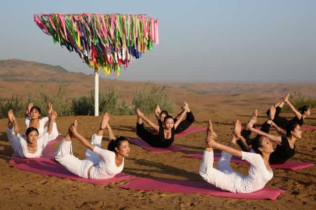 Dancers perform yoga in Xiangshawan Desert, also called Sounding Sand Desert on July 19, 2013 in Ordos of Inner Mongolia Autonomous Region, China. Xiangshawan is China's famous tourist resort in the desert. It is located along the middle section of Kubuqi Desert on the south tip of Dalate League under Ordos City. Sliding down from the 110-metre-high, 45-degree sand hill, running a course of 200 metres, the sands produce the sound of automobile engines, a natural phenomenon that nobody can explain. (Photo by Feng Li/Getty Images)