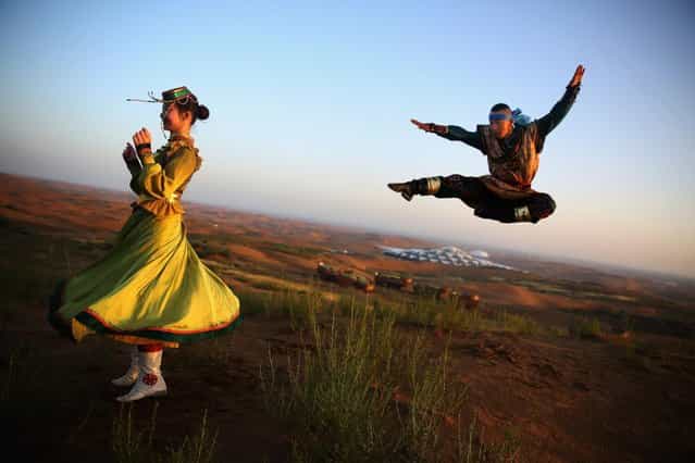 Dancers in traditional costumes perform near Desert Lotus Hotel in Xiangshawan Desert, also called Sounding Sand Desert on July 19, 2013 in Ordos of Inner Mongolia Autonomous Region, China. Xiangshawan is China's famous tourist resort in the desert. It is located along the middle section of Kubuqi Desert on the south tip of Dalate League under Ordos City. Sliding down from the 110-metre-high, 45-degree sand hill, running a course of 200 metres, the sands produce the sound of automobile engines, a natural phenomenon that nobody can explain. (Photo by Feng Li/Getty Images)