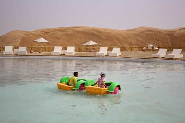 Two lillte boys play in a pool in Xiangshawan Desert, also called Sounding Sand Desert on July 18, 2013 in Ordos of Inner Mongolia Autonomous Region, China. Xiangshawan is China's famous tourist resort in the desert. It is located along the middle section of Kubuqi Desert on the south tip of Dalate League under Ordos City. Sliding down from the 110-metre-high, 45-degree sand hill, running a course of 200 metres, the sands produce the sound of automobile engines, a natural phenomenon that nobody can explain. (Photo by Feng Li/Getty Images)