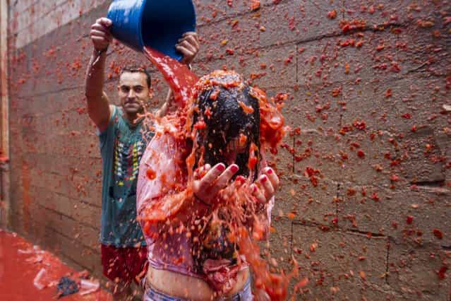 A young man throws a bucket of squashed tomatoes to a friend during the traditional tomato fight [Tomatina] during the fiestas in Bunol, Spain, 28 August 2013. This year's Tomatina is the first pay festival after Bunol's City Hall sold 15,000 tickets to take part in the tomato throwing. A total of 20,000 people, including 5,000 residents, will throw over 130,000 kg tomatoes. Local authorities decided to sell tickets this year to avoid the overcrowding in previous years in which over 50,000 people took part in the event. (Photo by Biel Alino/EPA)