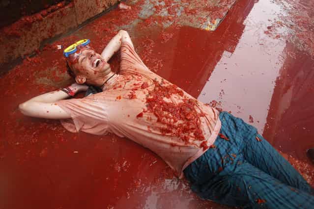 A man lays on a puddle of tomato during the annual [tomatina] tomato fight fiesta in the village of Bunol, 50 kilometers outside Valencia, Spain, Wednesday, August 28, 2013. Thousands of people are splattering each other with tons of tomatoes in the annual [Tomatina] battle in recession-hit Spain, with the debt-burdened town charging participants entry fees this year for the first time. Bunol town says some 20,000 people are taking part in Wednesday's hour-long street bash, inspired by a food fight among kids back in 1945. Participants were this year charged some 10 euros ($13) to foot the cost of the festival. Residents do not pay. (Photo by Alberto Saiz/AP Photo)