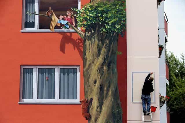 Steve Rolle paints the final element next to a trompe l'oeil depicting a woman and a squirrel at a window that are among features painted on the facade of the Wohngenossenschaft Soldaritaet coop apartment buildings as part of a 22,000 square meter mural in Berlin, on August 20, 2013. A group of artists working for French-based Citecreation painted the facades of the three buildings in imagery inspired by a nearby zoo and in cooperation with the buildings' residents. (Photo by Sean Gallup/Getty Images)
