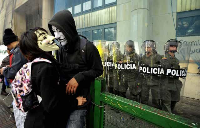 Masked protesters stand near police guarding a public building during a rally in Bogota, Colombia, on August 29, 2013. Students are protesting in support of farmers who demand lower fertilizer prices, complain of being undercut by cheap imports from near and far of products including potatoes, onions and milk, and say their sector is being hurt by free trade and other agreements promoted by the government. (Photo by Carlos Julio Martinez/Associated Press)