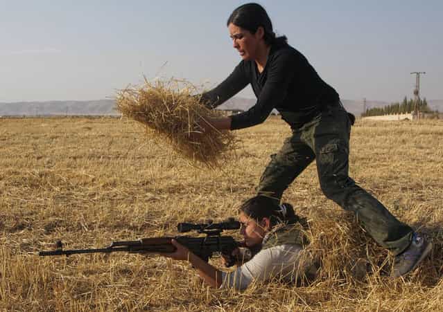 A Young Syrian-Kurdish woman hides a participant with hay in a training session organized by the Kurdish Women's Defense Units (YPJ) on August 28, 2013, in the northern Syrian border village of al Qamishli, to prepare them to defend their villages if they come under attack. (Photo by Benjamin Hiller/AFP Photo)