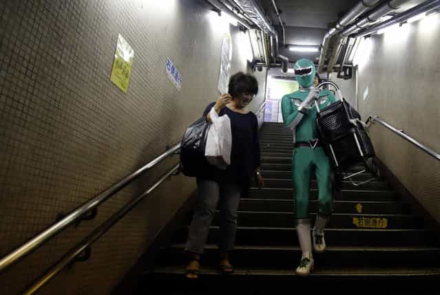 Tadahiro Kanemasu a.k.a the "Carry-Your-Pram-Ranger" carries a woman's shopping cart at the station in Tokyo August 23, 2013. In a green outfit with silver trim and matching mask, a superhero waits by the stairs of a Tokyo subway station, lending his strength to the elderly, passengers lugging heavy packages and mothers with baby strollers. (Photo by Yuya Shino/Reuters)