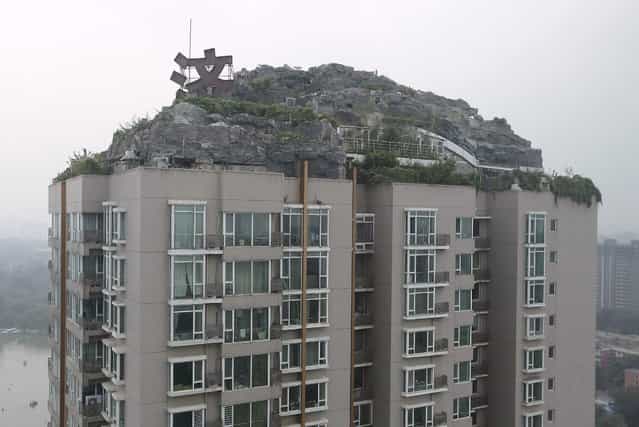 A privately built villa, surrounded by imitation rocks, is pictured on the rooftop of a 26-storey residential block in Beijing, August 13, 2013. A resident in the building has spent more than six years to build a villa covering over 1,000 square meters (10,764 square feet) on top of a 26-storey building in Beijing, according to local media. Residents in the building complained about the villa, fearing its weight may cause structural collapse. The local bureau of city administration attempted to investigate the allegedly illegal construction, but the owner has not shown up so far, Xinhua News Agency reported. (Photo by Jason Lee/Reuters)