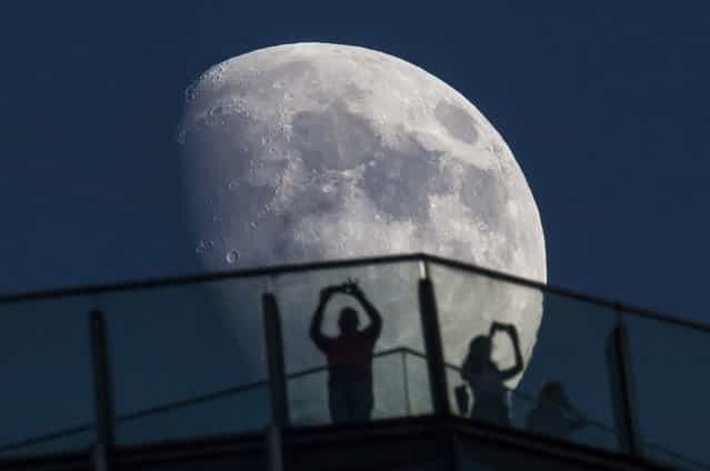 Visitors stand on the roof of a skyscraper as the moon rises over the skyline in Shanghai, on August 16, 2013. (Photo by Aly Song/Reuters)