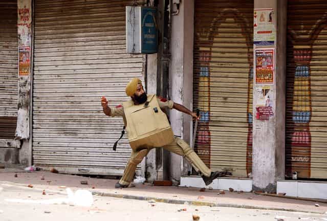 A policeman throws stones at Hindus protesting against the state government after rival communities clashed in Kishtwar, in Jammu, India, on August 10, 2013. Indian forces fired warning shots Saturday to enforce a curfew and to push angry people back into their homes in Kishtwar, in the Indian portion of Kashmir where clashes between Muslims and Hindus during Eid celebrations killed at least two people and injured another 24. (Photo by Channi Anand/Associated Press)