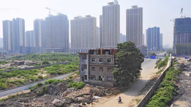 A man rides his bicycle past a partially demolished building in the middle of a street next to residential construction sites in Xi'an, August 14, 2013. A family of 7 still lived in the three-storey building without electricity and water after a demolition project in the region took place in 2010. According to local media, the owner of the house refused to move as a protest against a land dispute lawsuit between him and his brother, which he lost. (Photo by Reuters/Stringer)