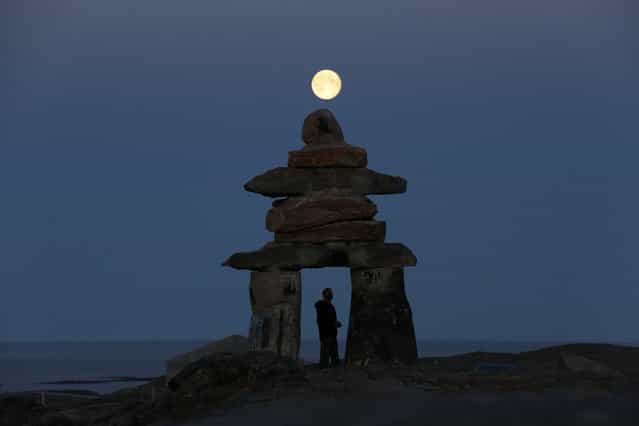 A man looks at a giant inukshuk as the moon rises above it in Rankin Inlet, Nunavut, Canada, on August 21, 2013. The inukshuk is a stone landmark or cairn used by the Inuit people in the arctic. (Photo by Chris Wattie/Reuters)