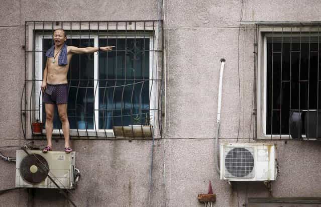 A man, whose last name is Hou, gestures while holding a knife as he stands outside a window atop an air conditioner theatening to cut himself, in Anshan, Liaoning province August 26, 2013. (Photo by Reuters/Stringer)