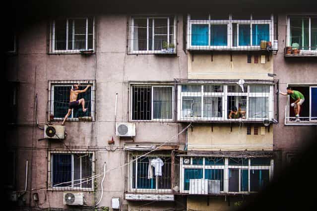 A man climbs outside a window with a knife, as his mother and a plain clothes policeman look watch him in Anshan, Liaoning province, China, on August 26, 2013. He held his mother captive in his apartment before climbing out of the window and threatening to cut himself. After several hours, he was controlled by policemen who managed to enter the house from another window with the help of his mother, local media reported. (Photo by Reuters)