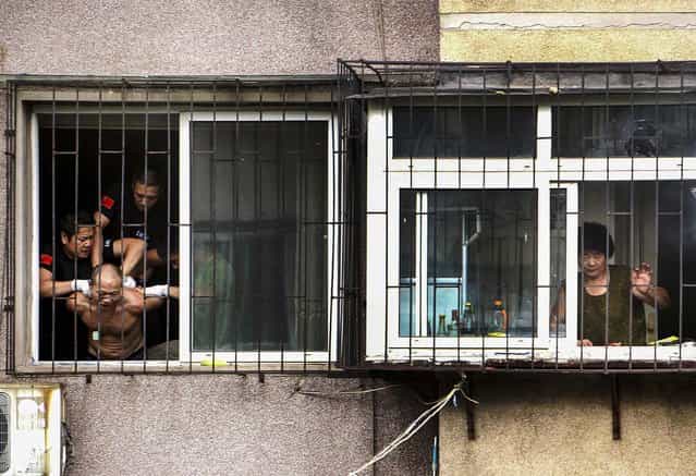 Police grab a man after he threatened to cut himself in Anshan, Liaoning province. The man held his mother captive in his apartment before climbing out of the window and threatening to harm himself. (Photo by Reuters)