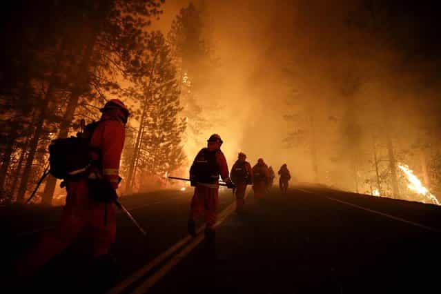 Inmate firefighters walk along state Highway 120 as firefighters continue to battle the Rim Fire near Yosemite National Park, on August 25, 2013. Fire crews are clearing brush and setting sprinklers to protect two groves of giant sequoias as the massive week-old wildfire rages along the remote northwest edge of the park. (Photo by Jae C. Hong/Associated Press)