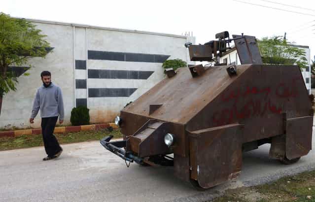 A Syrian rebel walks past Sham 2, a homemade armored vehicle, in Bishqatin, Syria, on December 8, 2012. From a distance it looks rather like a big rusty metal box but closer inspection reveals a homemade armored vehicle waiting to be deployed. Sham II, named after ancient Syria, is built from the chassis of a car and touted by rebels as [100 percent made in Syria]. (Photo by Herve Bar/AFP Photo)