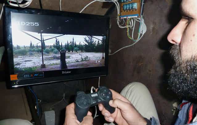 A Syrian rebel uses a videogame controller to activate the machine gun of Sham 2, a homemade armored vehicle made by the rebels' Al-Ansar brigade, in Bishqatin, 4 km west of Aleppo, on December 8, 2012. (Photo by Herve Bar/AFP Photo)
