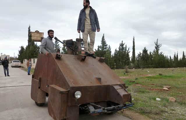 Syrian rebels stand atop Sham II, a homemade armoured vehicle made by the rebels' Al-Ansar brigade, in Bishqatin, 4 kms west of Aleppo, on December 8, 2012. The Sham II, which was cobbled together from the chassis of an old diesel car and parts salvaged from a junkyard in under a month, uses a controller from a Sony Playstation games console to aim a roof-mounted machine gun. Inside the rusting steel panels a crew of two sit side-by-side in front of flatscreen TV's mounted on the wall. Sham II, named after ancient Syria, touted by rebels as [100 percent made in Syria]. (Photo by Herve Bar/AFP Photo)