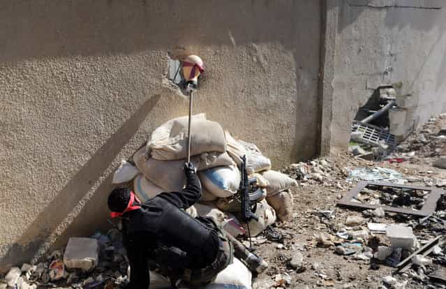 A [Free Syrian Army] fighter holds the head of a mannequin up to a hole in a wall of a Syrian Army base to attract and locate a sniper during heavy fighting in the Arabeen neighborhood of Damascus, on February 3, 2013. (Photo by Goran Tomasevic/Reuters)