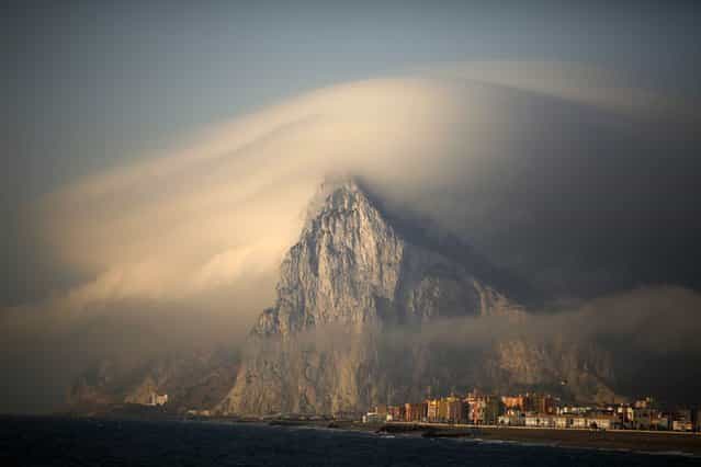 A cloud partially covers the tip of the Rock of the British territory of Gibraltar at sunrise from La Atunara port before Spanish fishermen sail in their fishing boats with their relatives to take part in a protest at an area of the sea where an artificial reef was built by Gibraltar using concrete blocks, in Algeciras bay, La Linea de la Concepcion in southern Spain August 18, 2013. For just over an hour some 30 fishing boats circled where 70 3-tonne concrete blocks were dropped in July to form a reef that Spain said was not legal and prompted the government to ramp up border checks with the British overseas territory. (Photo by Jon Nazca/Reuters)