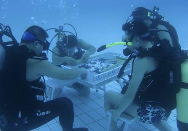 Diving instructors play mahjong in a swimming pool in Xiangtan, Hunan province August 9, 2013. According to local media, the trainers re-invented the game of mahjong by playing it under water in a 5.5-metre-deep pool to escape from the summer heat, and since then more than 10 divers have been playing the game. China's top meteorological authority on Tuesday continued to warn of prolonged heat that has afflicted central and eastern China since July, Xinhua News Agency reported. (Photo by Reuters/Stringer)