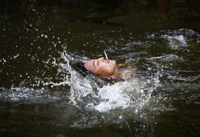 A devotee smokes a cigarette as he swims during the Deopokhari festival in Khokana August 23, 2013. During the annual festival, a live goat is thrown into a pond and the team of devotees that retrieves the animal first wins. (Photo by Navesh Chitrakar/Reuters)