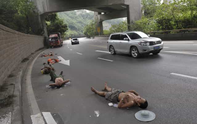 Labourers who work nearby nap on a road as cars drive past in Chongqing Municipality, July 23, 2013. (Photo by Reuters/Stringer)