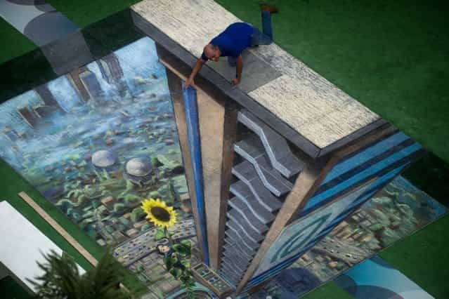 A man poses by the work of British artist Julian Beever, specialized in pavement drawings, wall murals and realistic paintings, made in a shopping center in Medellin, Antioquia department, Colombia, on September 6, 2013. (Photo by Raul Arboleda/AFP Photo)