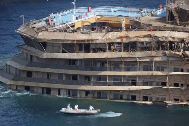 Workers on a boat sail past the Costa Concordia ship after it was lifted upright, on the Tuscan Island of Giglio, Italy, Tuesday, September 17, 2013. Engineers declared success on Tuesday as the Costa Concordia cruise ship was pulled completely upright during a complicated, 19-hour operation to wrench it from its side where it capsized last year off Tuscany, an unprecedented feat that sets the stage for it to be towed away next year. (Photo by Andrew Medichini/AP Photo)