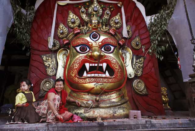 A Nepalese woman and a girl sit in front of a statue of Hindu deity Swet Bhairav during the last day of the week-long Indra Jatra festival in Katmandu, Nepal, Monday, September 16, 2013. The festival marks the end of the monsoon season and beginning of autumn. (Photo by Niranjan Shrestha/AP Photo)
