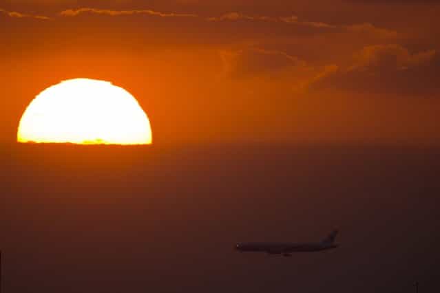 A passenger jet flies past the setting sun in Shanghai September 17, 2013. (Photo by Reuters)