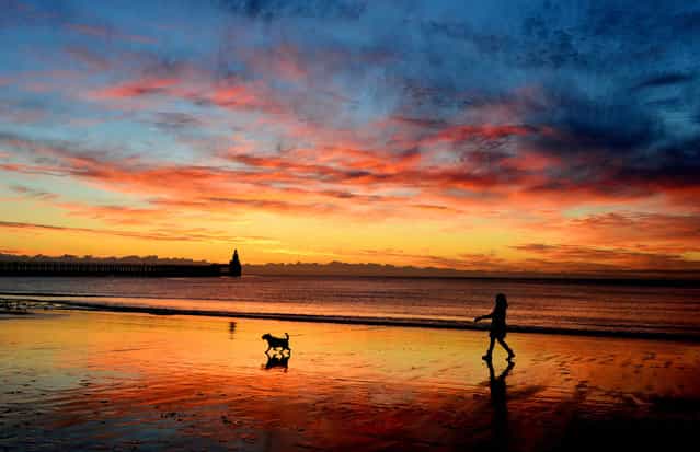 A woman walks her dog at sunrise on Blyth beach, Northumberland, September 18, 2013. (Photo by Owen Humphreys/PA Wire)