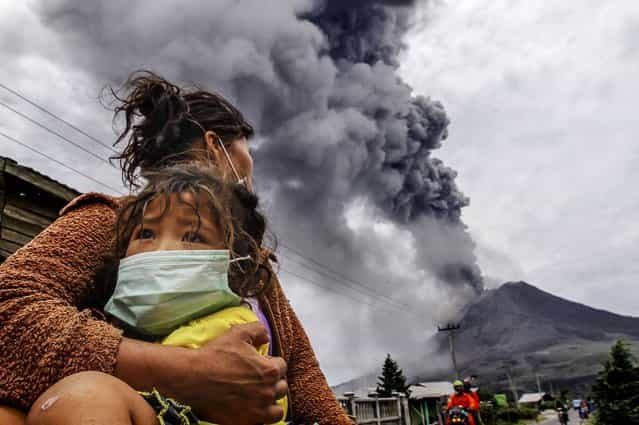 A mother holds her child as Mount Sinabung spews ash and hot lava during an eruption in Perteguhan village in Karo district, Indonesia's north Sumatra province, on September 17, 2013. (Photo by Roni Bintang/Reuters)