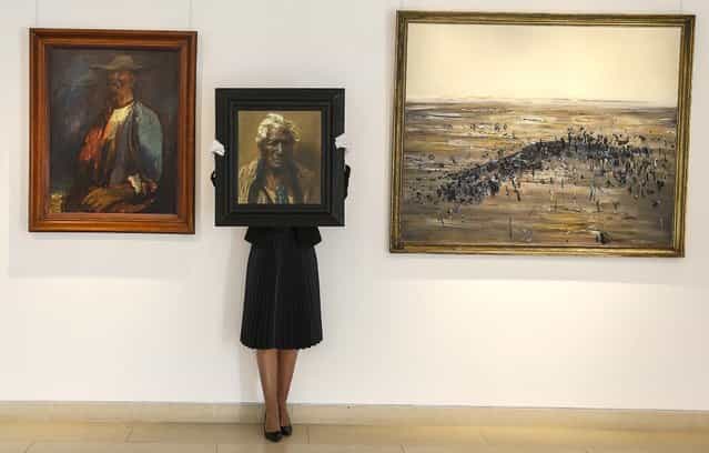 A Christie's employee holds the painting, [An Aristocrat, Atama Paparangi] by Charles Frederick Goldie, at left is [Old Larsen] by Sir George Russell Drysdale, and at right is [Lysterfield] by Frederick Ronald Williams, during a media tour at the auction rooms in London, on September 20, 2013. The painting is estimated at to bring between $321,000 and $481,000 Ul be during the Australian Art sale. (Photo by Kirsty Wigglesworth/Associated Press)