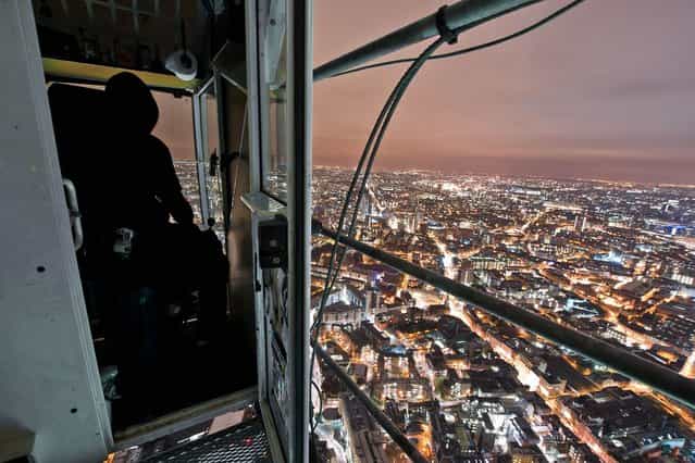 A hooded figures sits in a crane cab high above the city on the site of The Shard skyscraper in London. (Photo by Bradley L. Garrett/Barcroft Media)